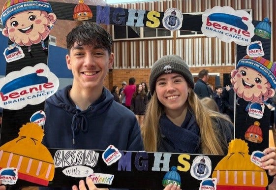 Two students holding beanie day sign at breakfast with a friend morning